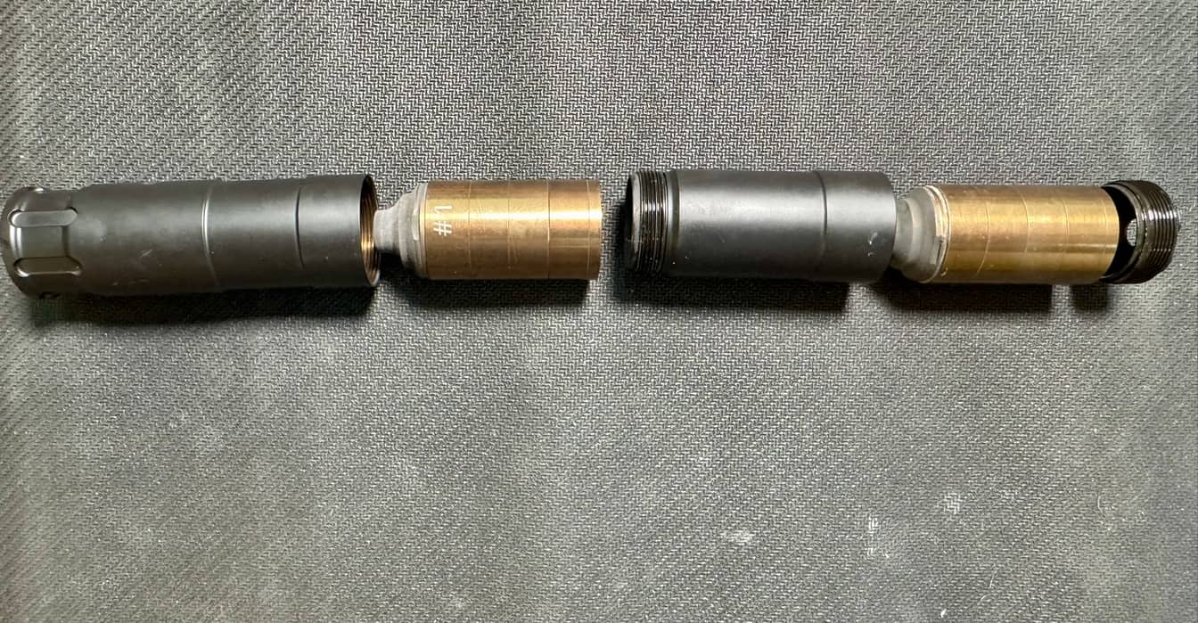 The Rugged Oculus22 separated into its two modules and laid end to end on grey fabric, showing the threaded joint and the brass-coloured baffle stacks inside each half.