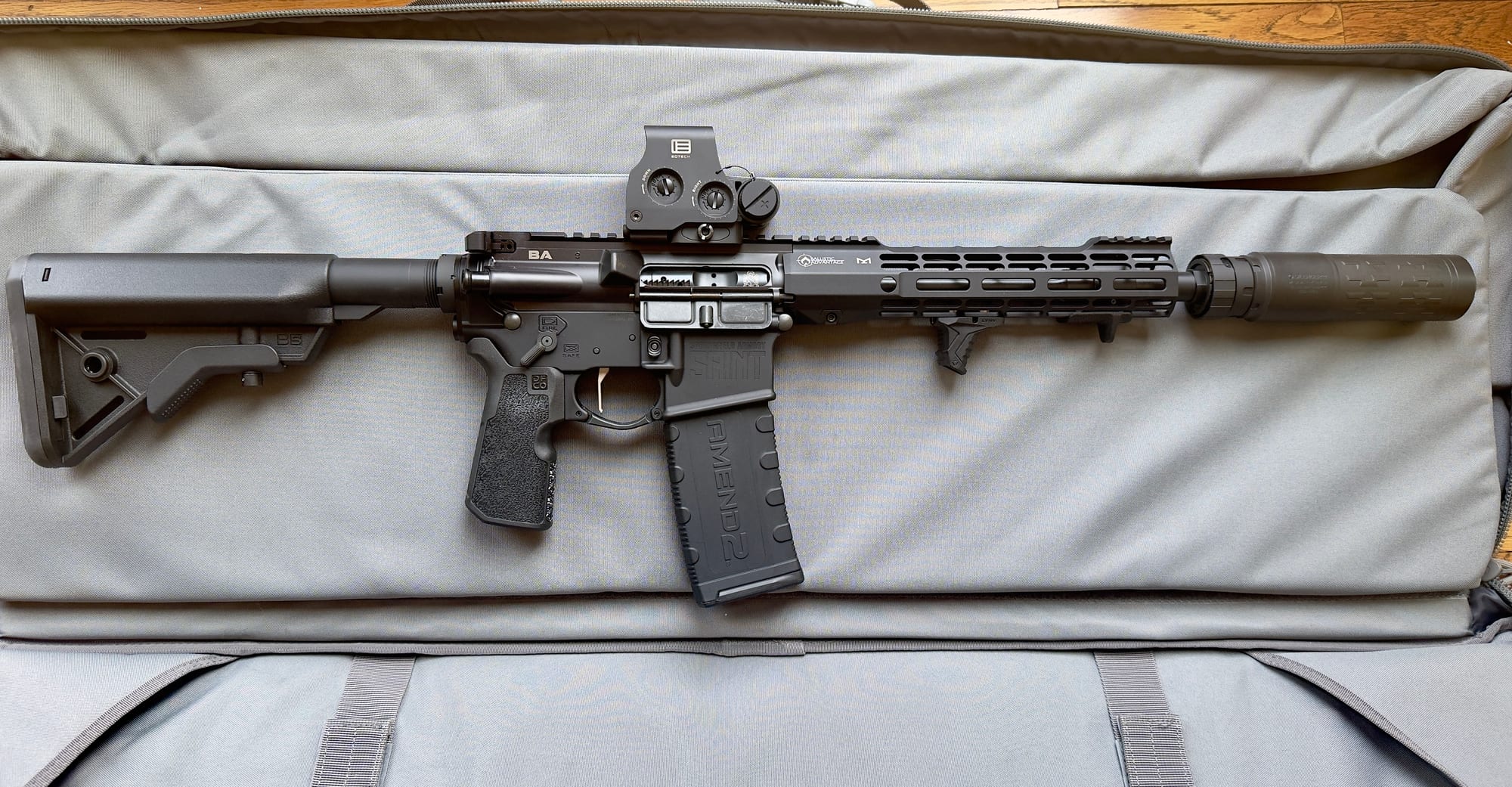 The SilencerCo Velos LBP 5.56 mounted on a 10.5-inch AR-15 built on a Springfield Armory SAINT Victor lower and a Ballistic Advantage upper, lying in an open grey rifle case on a wood floor.