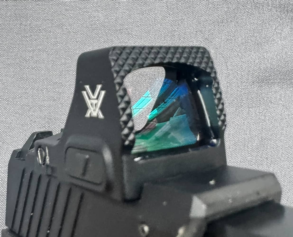 The Vortex Defender-CCW mounted on a pistol slide, photographed from the front, the window showing a strong blue and green coating and the front of the housing standing open.